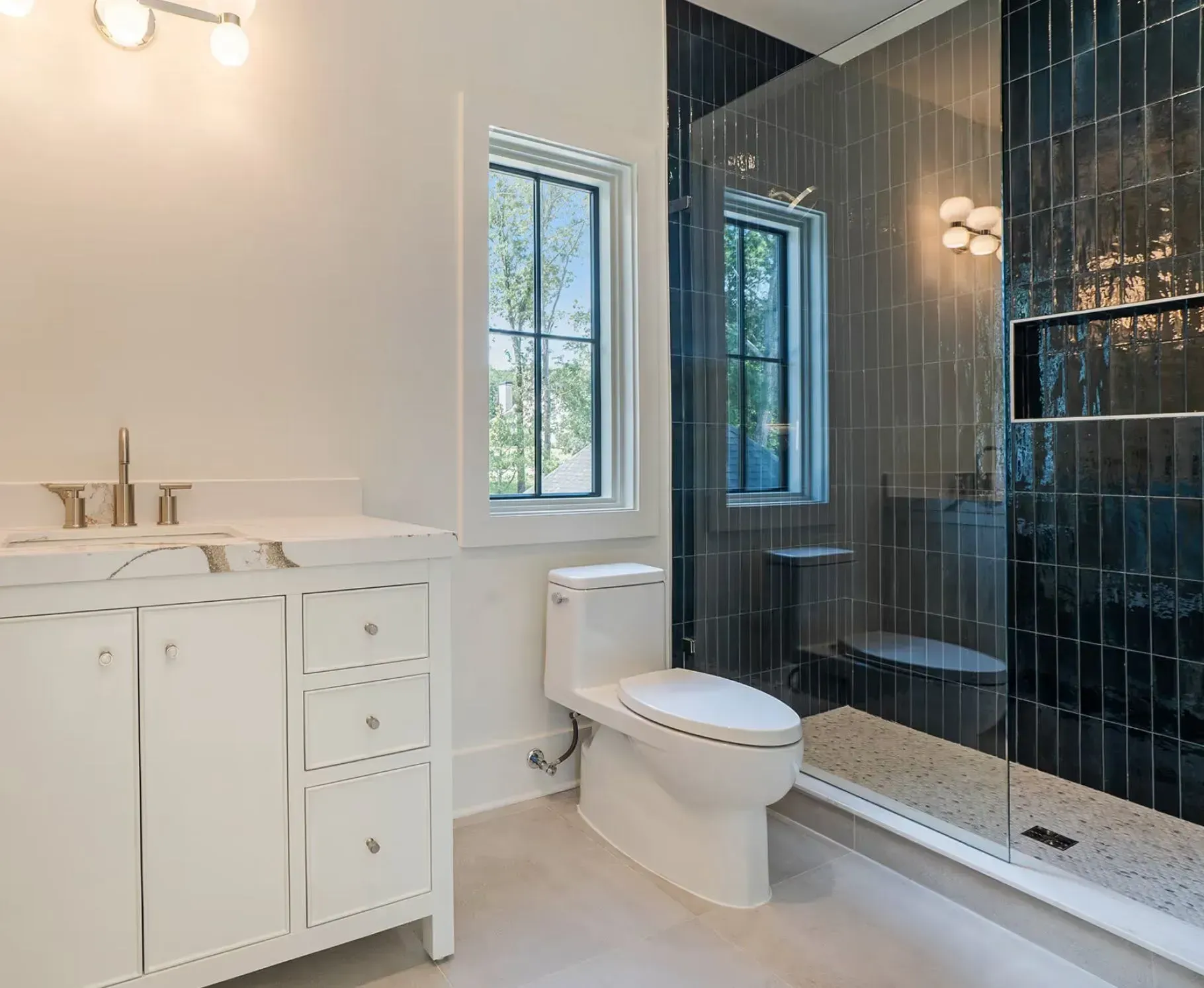 Modern bathroom with white vanity, toilet, and black glass shower tile, bright window light