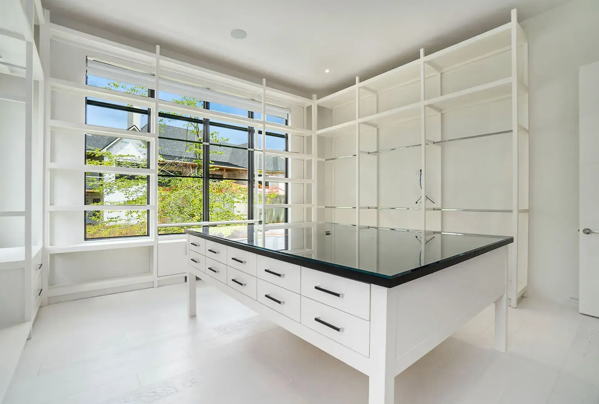 Bright white kitchen with island, black countertop, and built-in white shelving by large windows