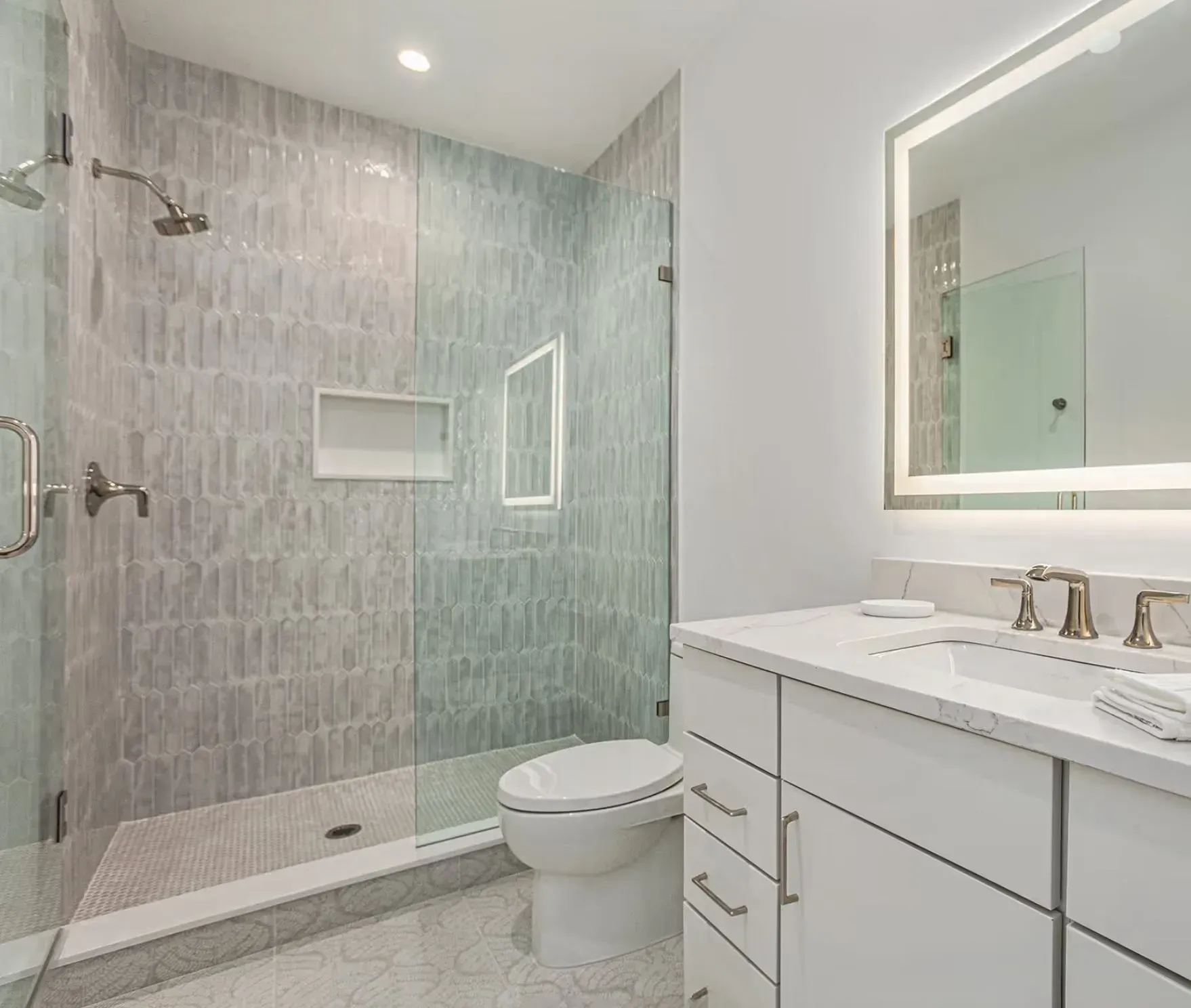 Modern white bathroom with walk-in shower, glass door, vanity, and lit mirror