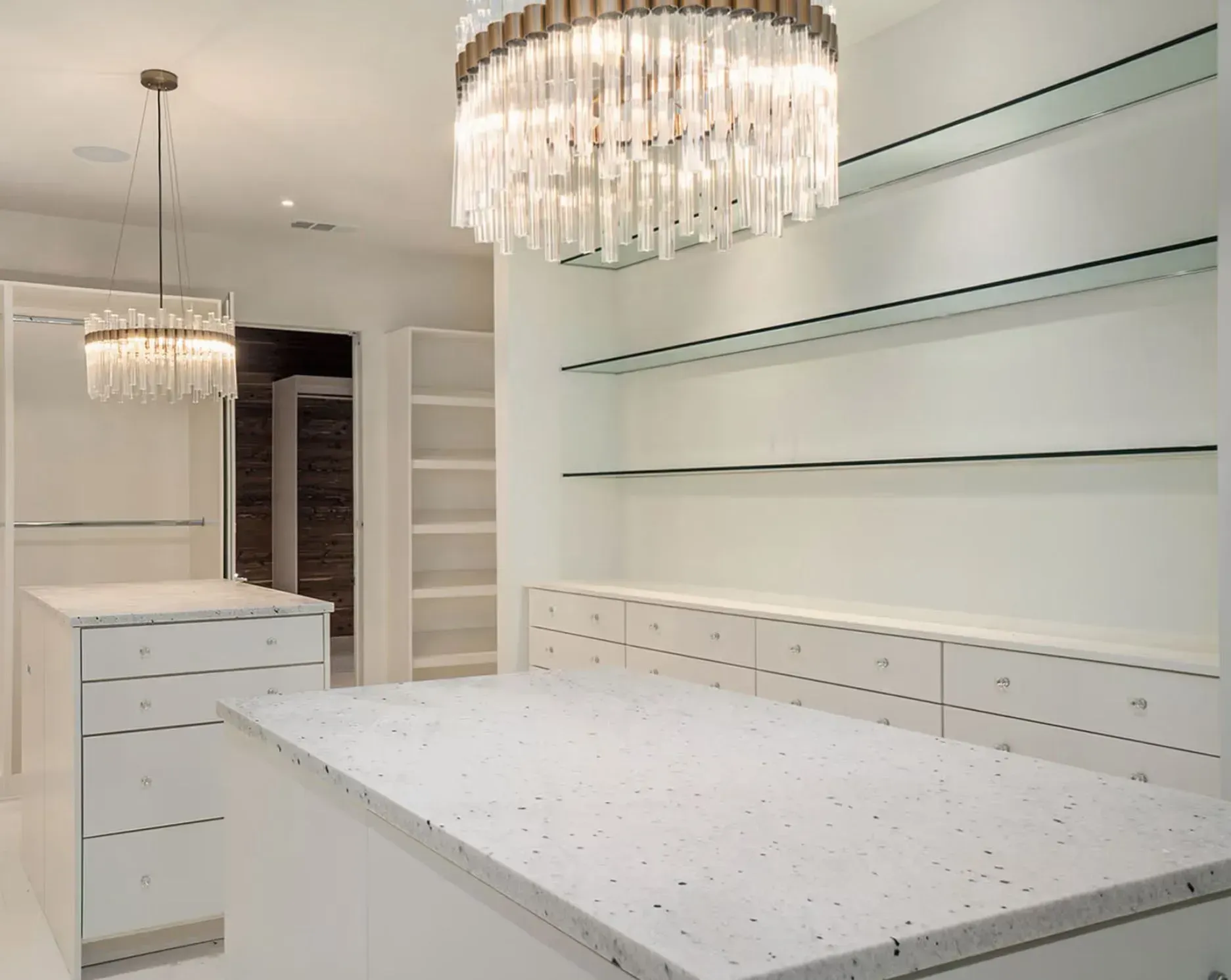 Bright white dressing room with chandelier, built-in shelves, and speckled countertops