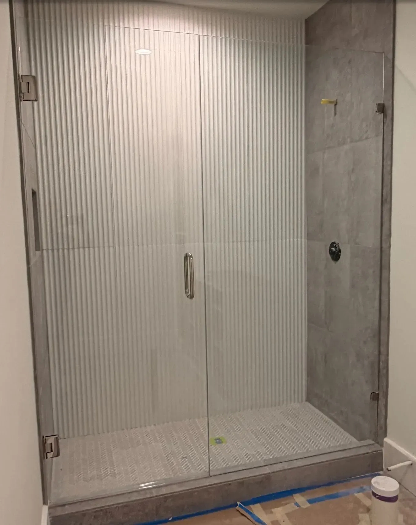 Glass shower stall with frosted doors, tiled walls, and a shower base under construction.