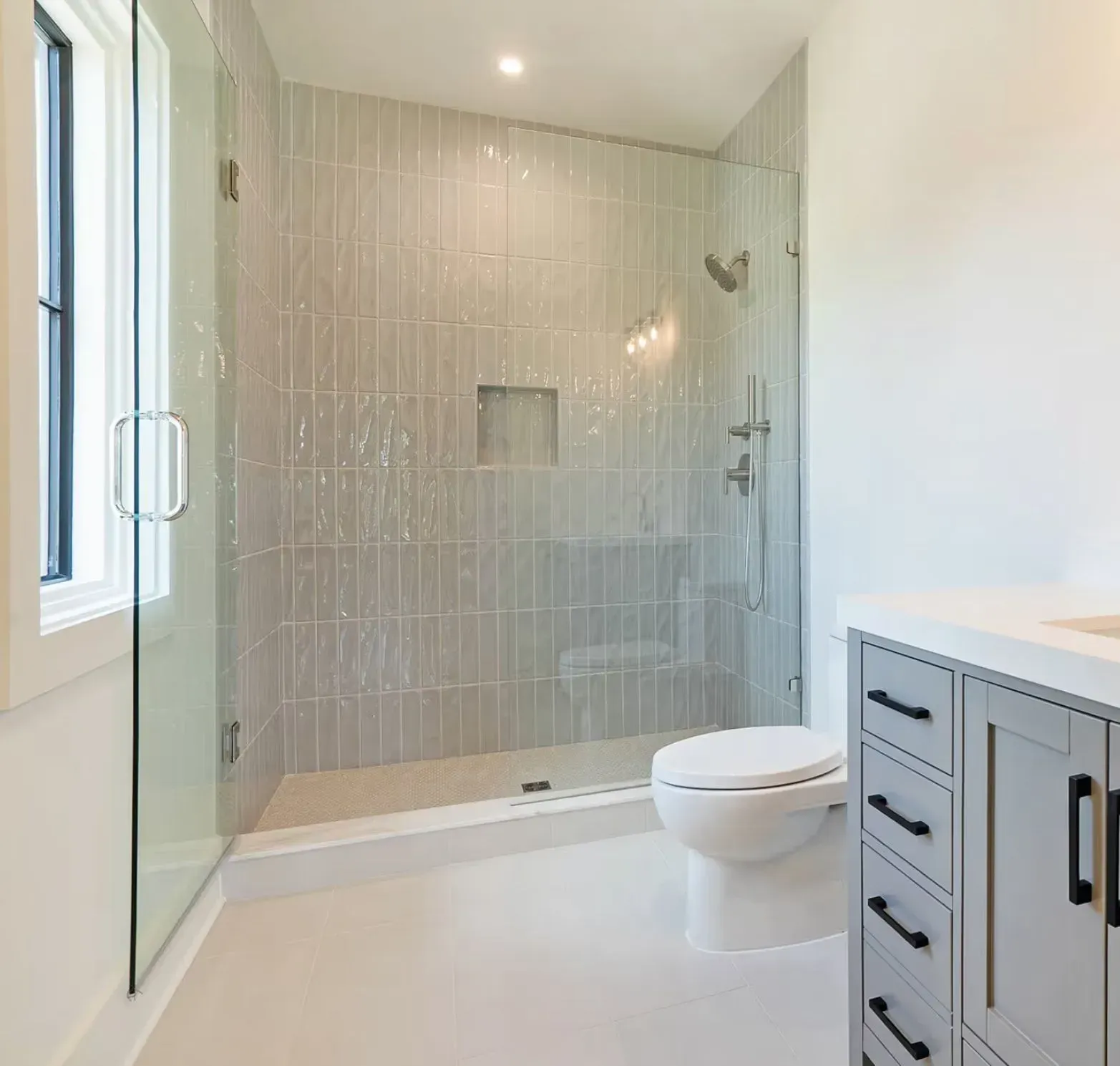 Modern white bathroom with glass walk-in shower, wall-mounted toilet, and gray vanity