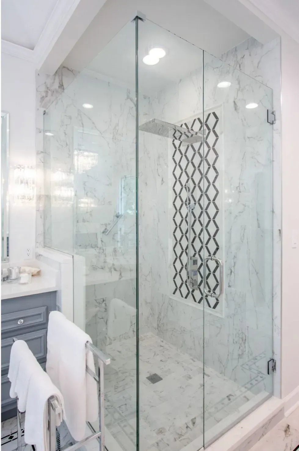 Glass-enclosed marble shower in a bright white bathroom with a decorative towel hanging inside