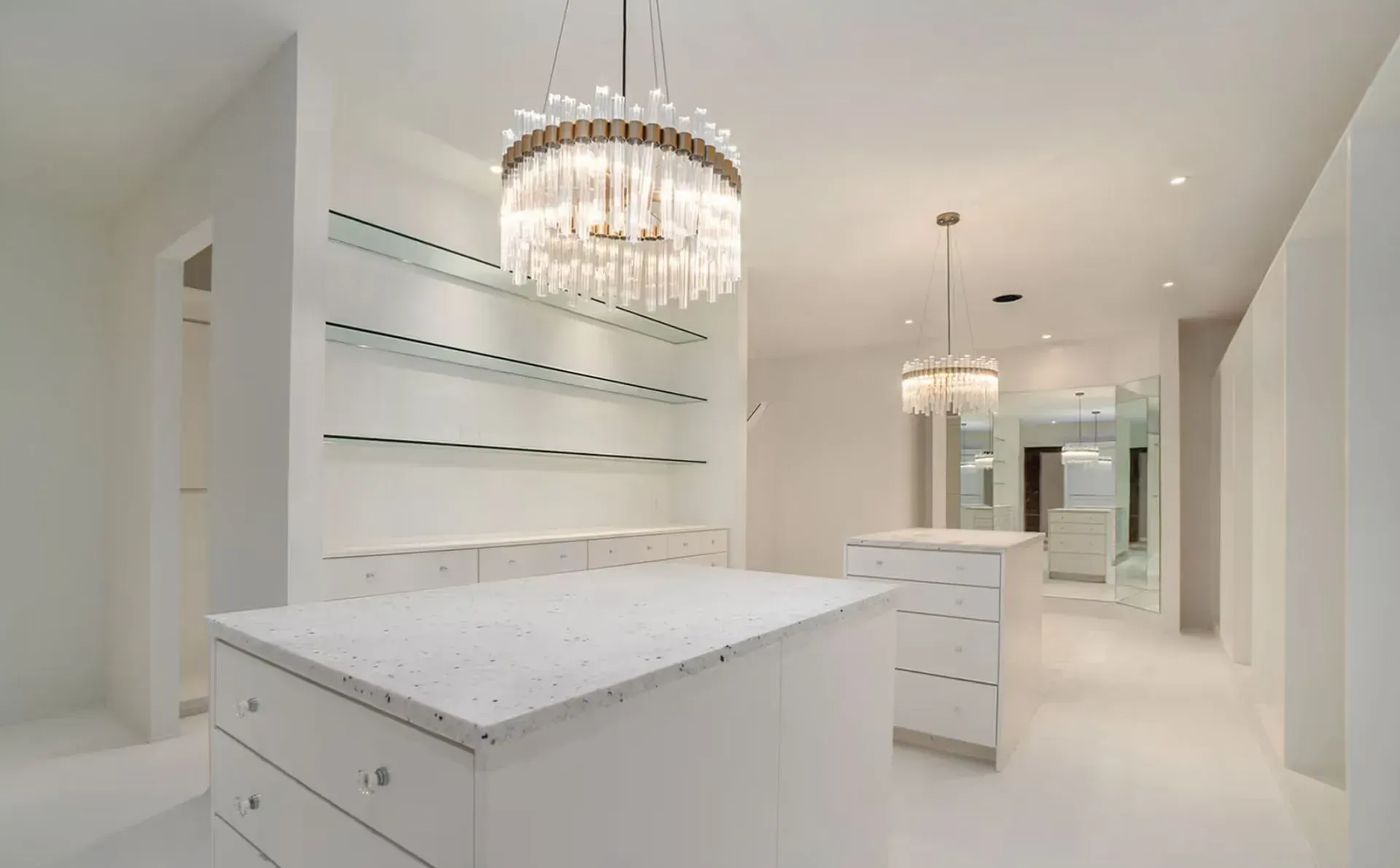 Modern white dressing room with built-in shelves, island drawers, and crystal chandeliers