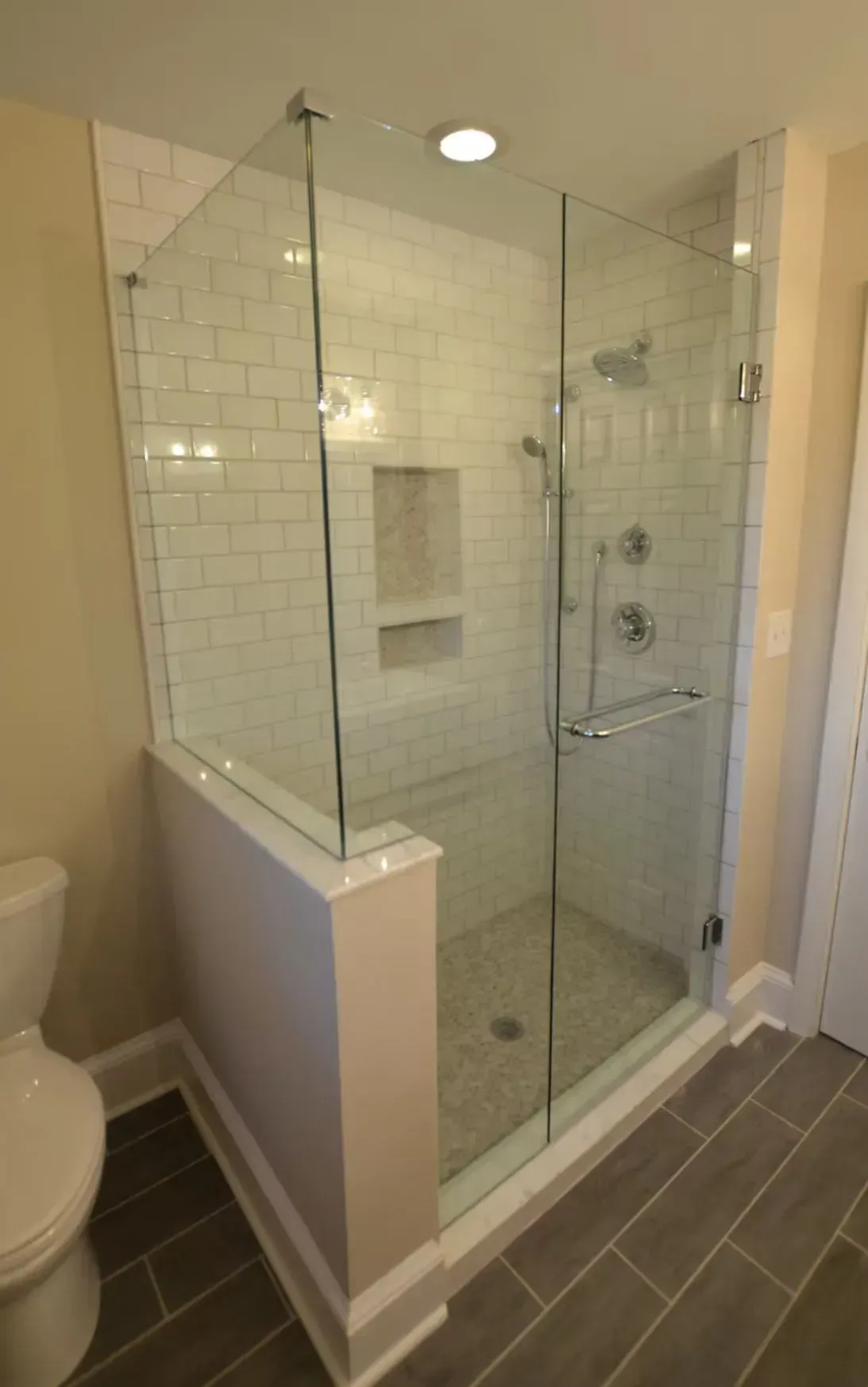 Glass walk-in shower with white subway tile, built-in shelf, and gray floor tiles in a bathroom