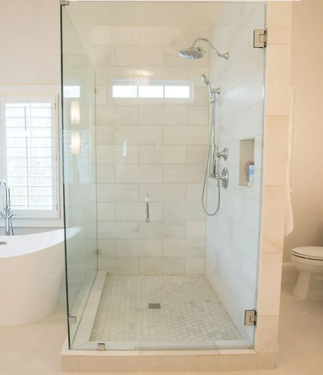Glass walk-in shower with white tile and built-in bathtub in a bright bathroom