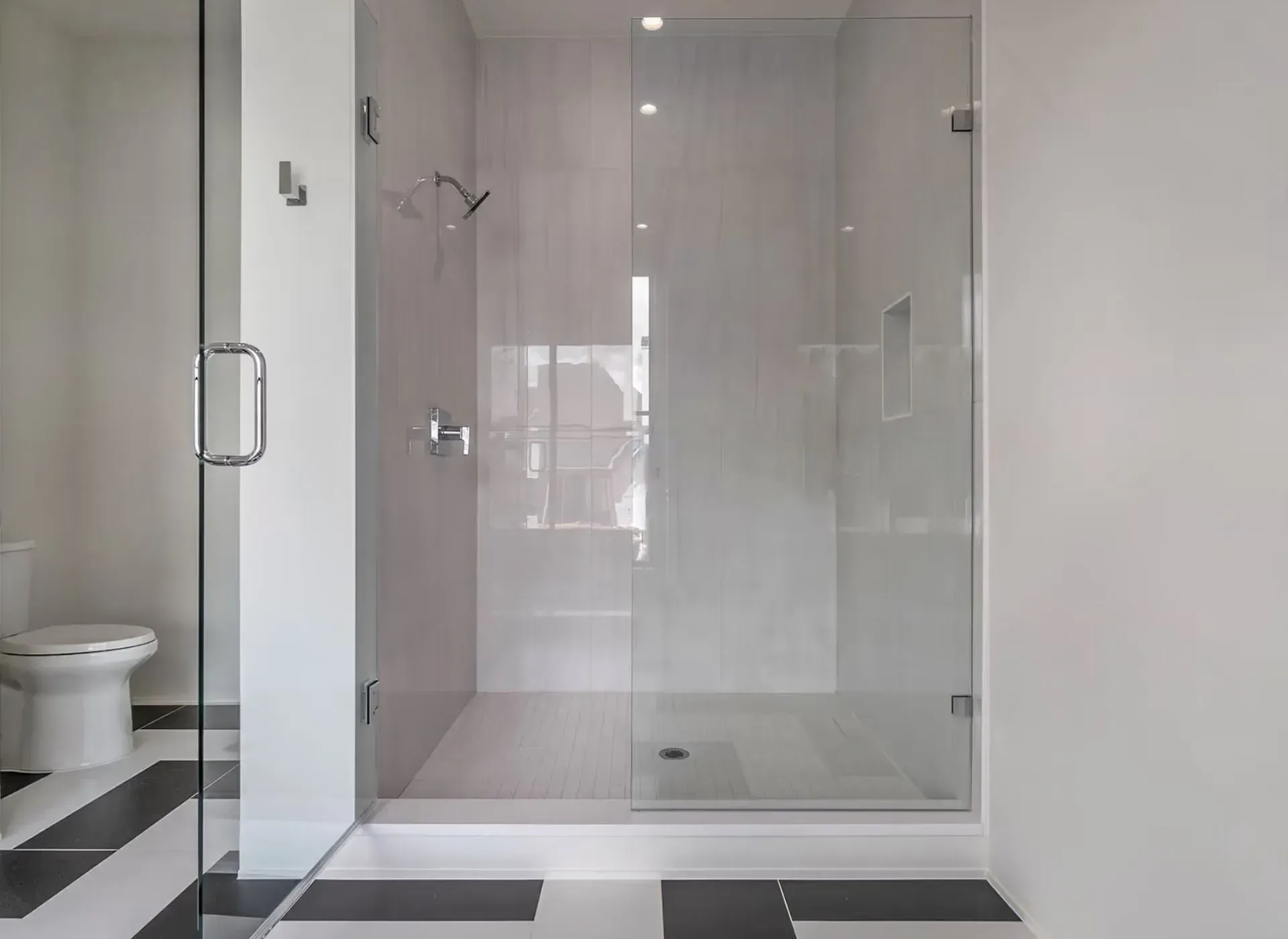 Modern bathroom with glass-enclosed shower, white tile walls, and black-and-white floor.