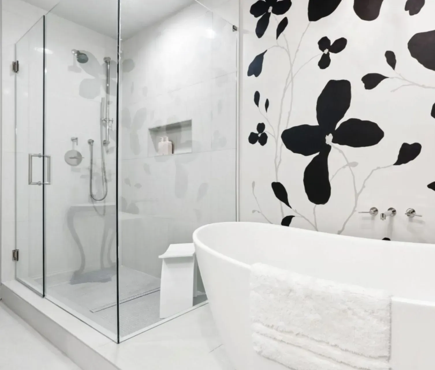 Modern white bathroom with glass shower, freestanding tub, and bold black floral wall tiles