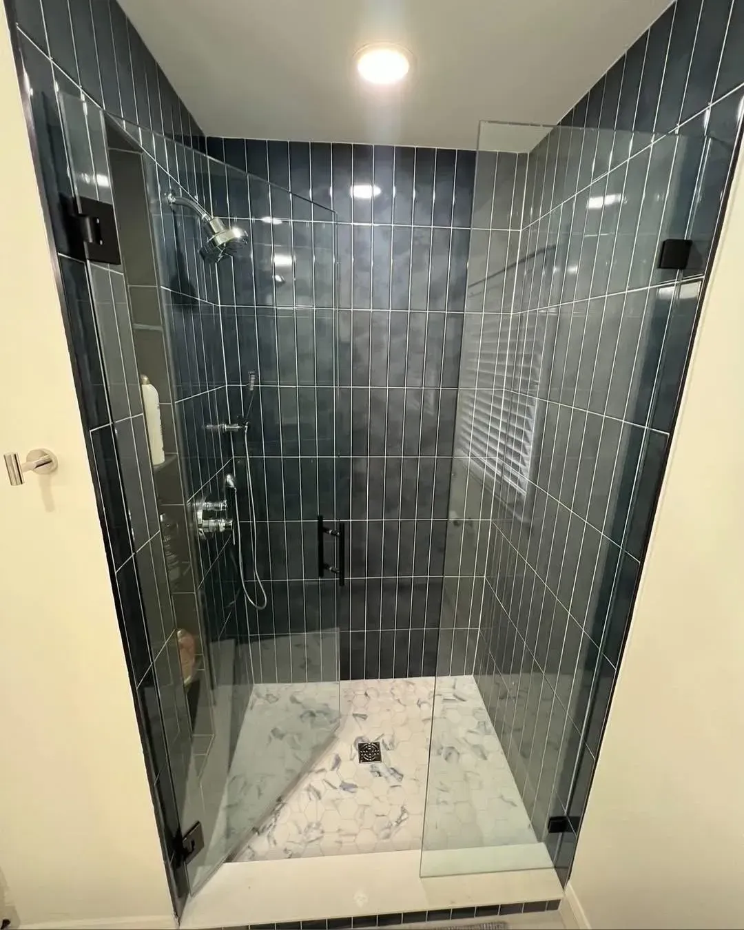 Empty tiled shower stall with glass door and dark gray wall tiles.