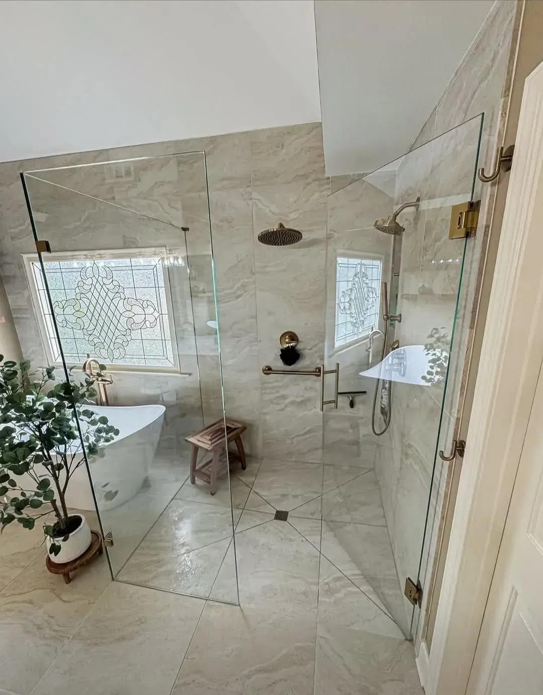 Modern bathroom with walk-in shower, freestanding tub, and large windows; a plant sits near the tub
