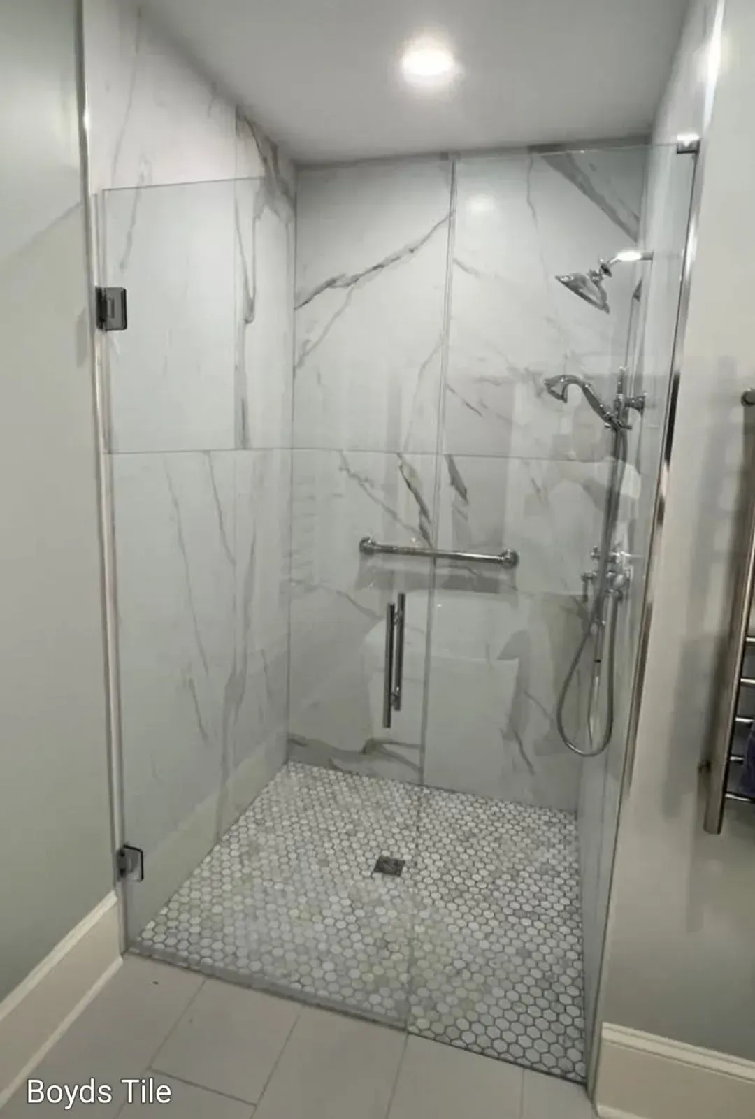 Modern glass shower with white marble-look walls, chrome fixtures, and pebble tile floor