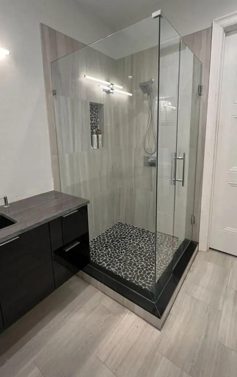 Glass shower enclosure with black pebble floor next to a dark vanity in a modern bathroom