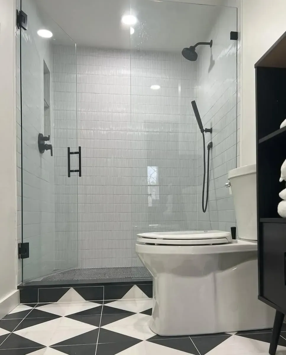 Modern bathroom with glass shower, white toilet, black-and-white floor, and shelving unit