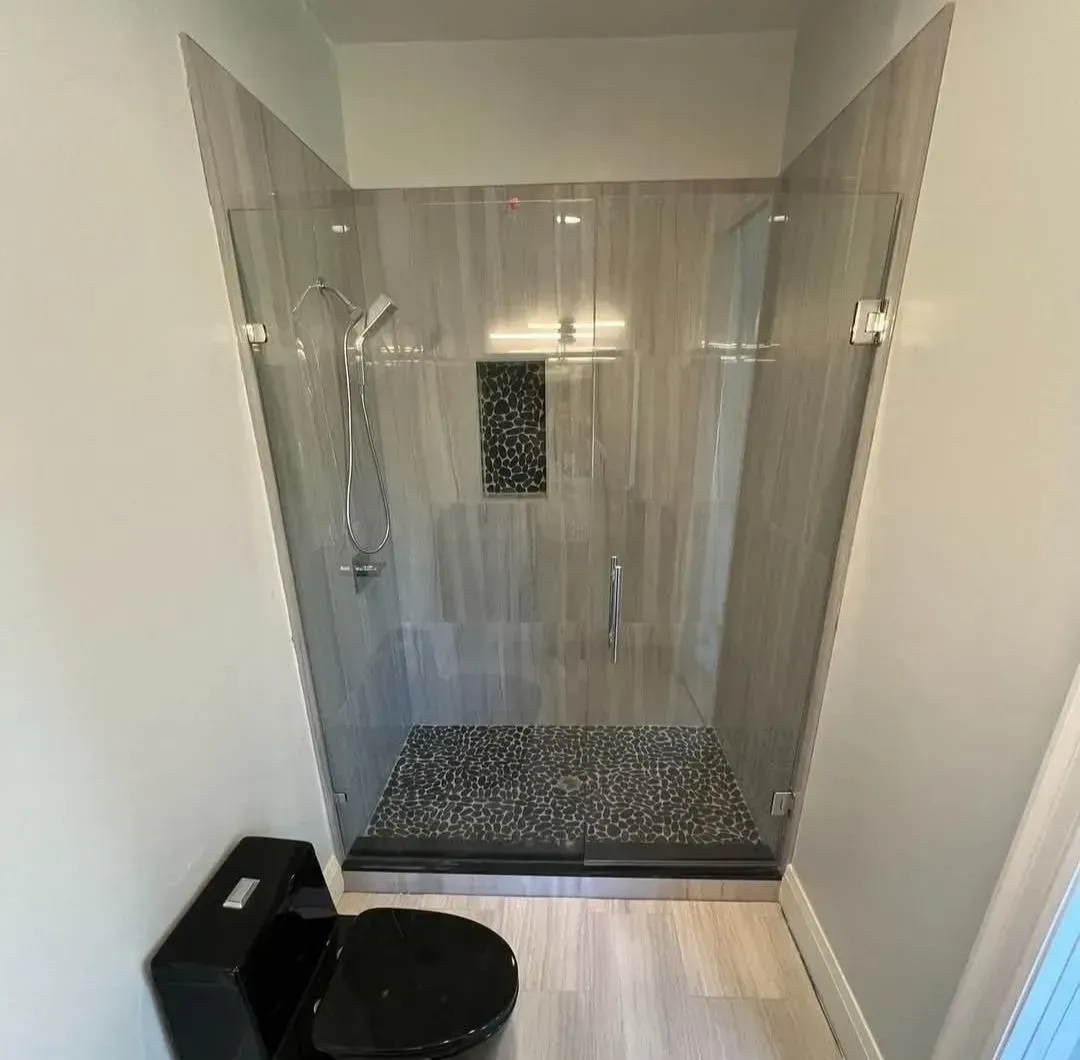 Small bathroom with a black toilet and a glass-enclosed shower stall with gray tile floor.