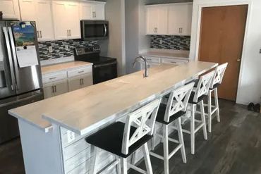 A kitchen with a long island , stools and a refrigerator.