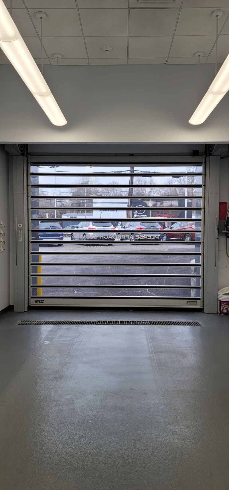 An empty garage with a garage door open and a parking lot in the background.