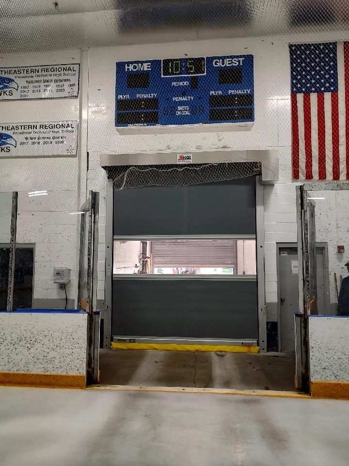 A hockey rink with a scoreboard and an american flag on the wall.