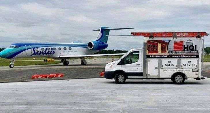 A white van is parked next to an airplane on a runway.