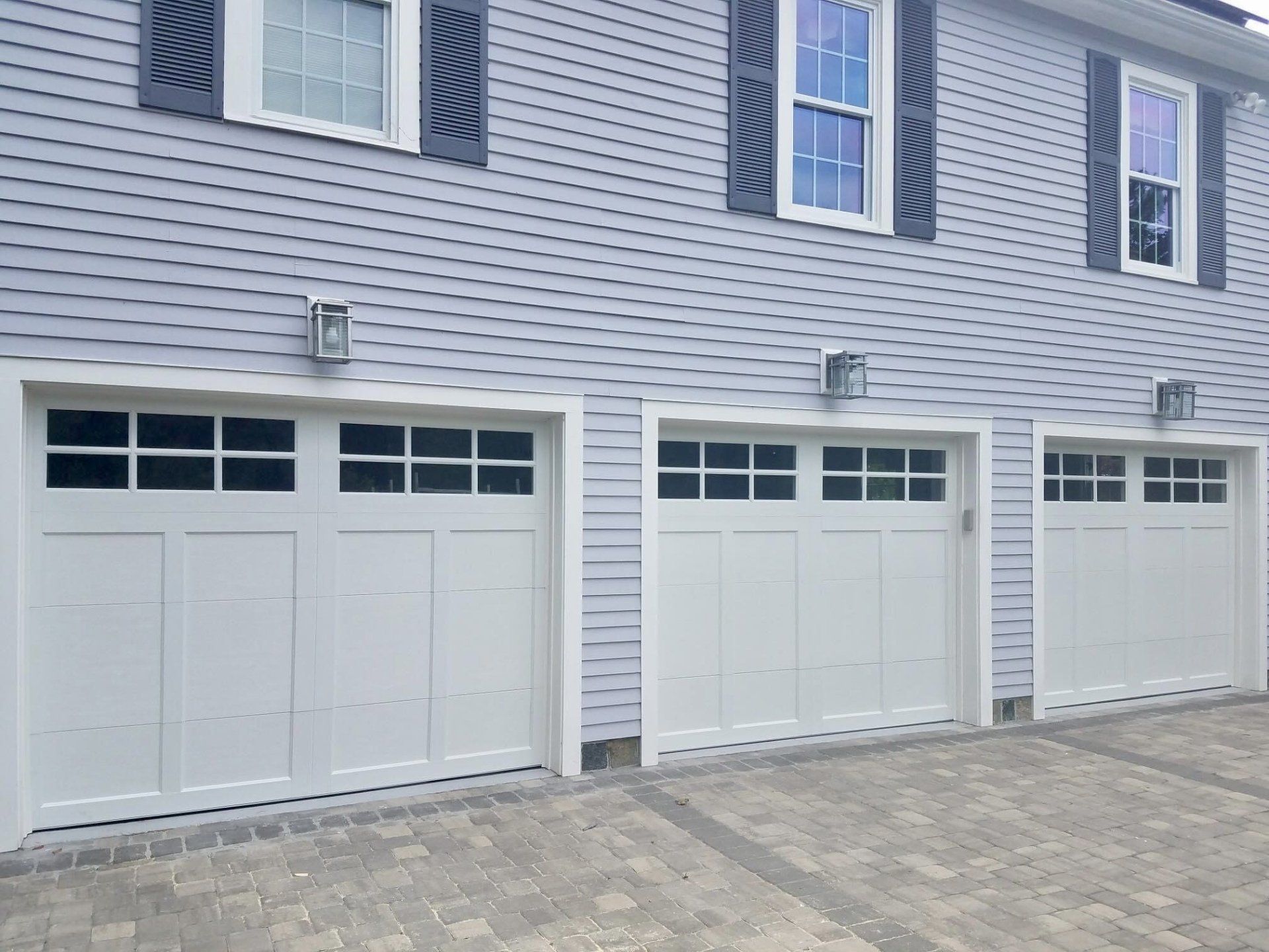 A row of white garage doors on the side of a house.