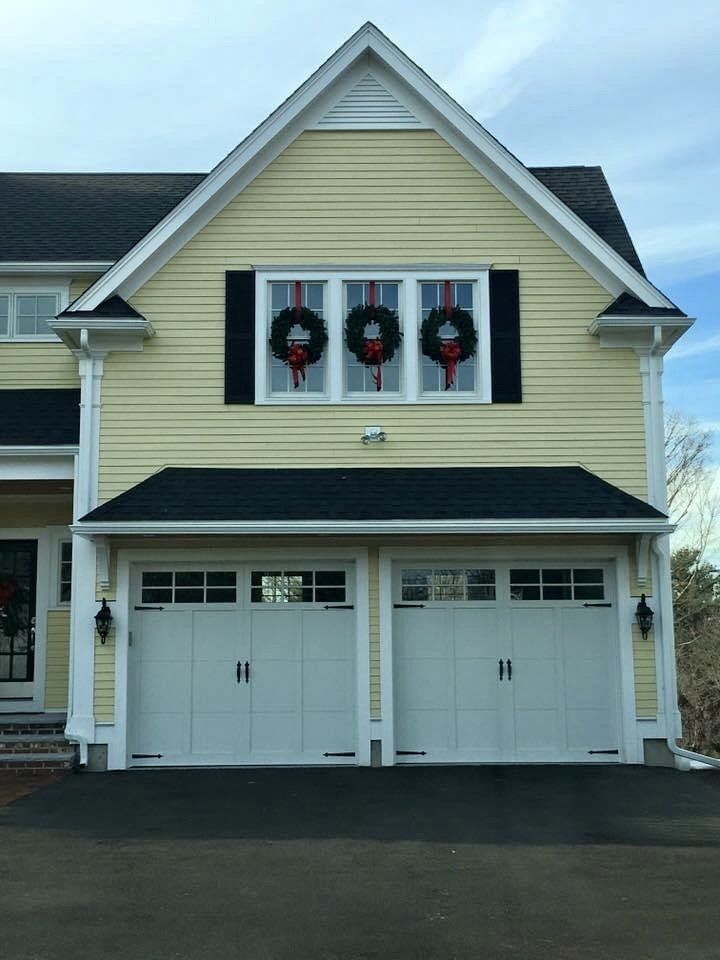 A yellow house with white garage doors and christmas wreaths on the windows