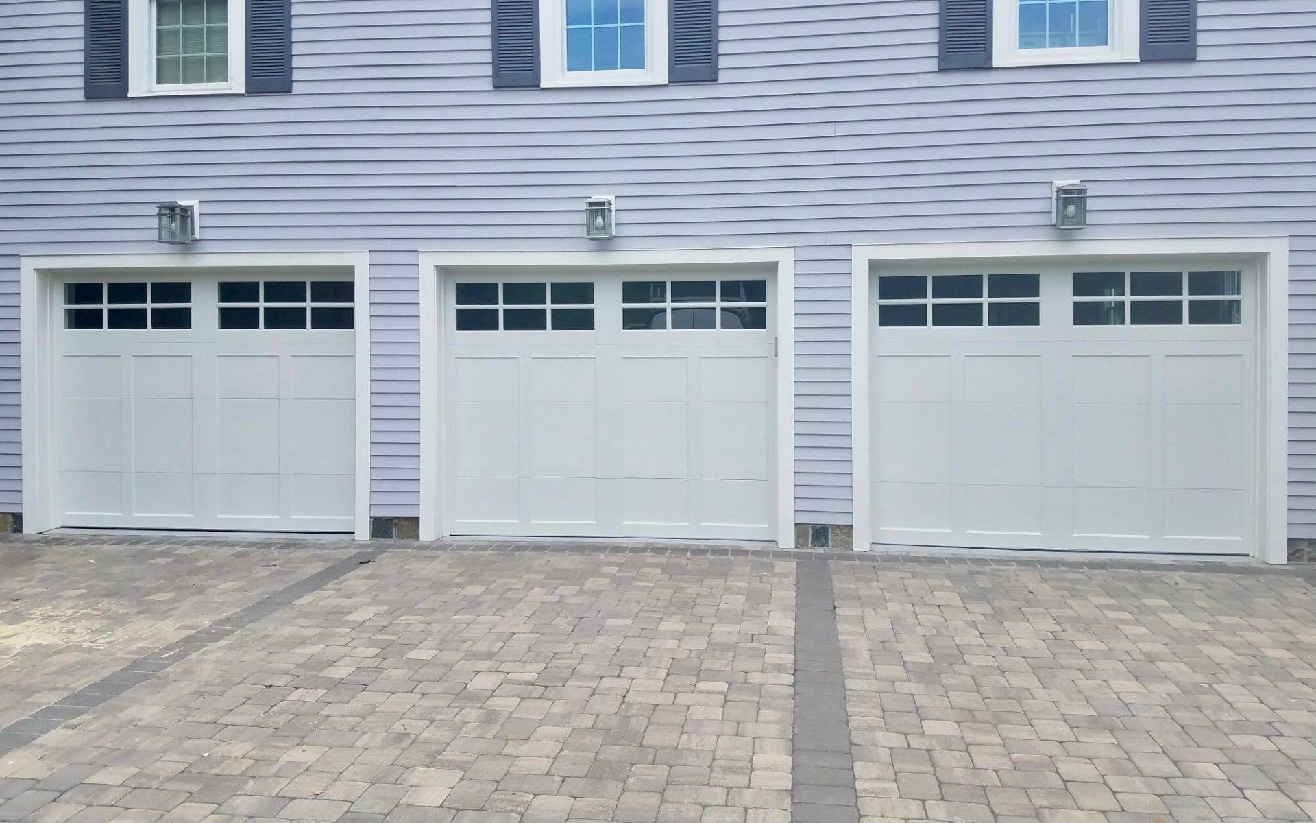 Three white garage doors are lined up in front of a purple house.