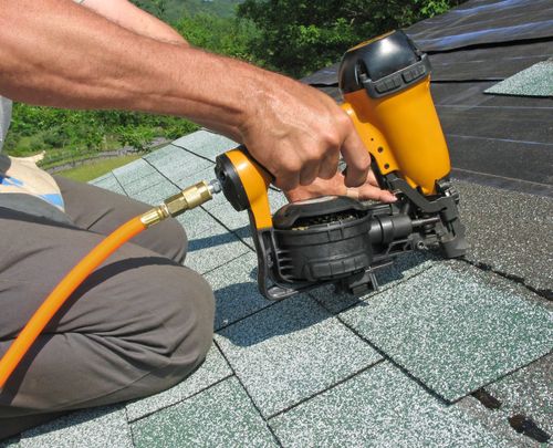 Worker using a pneumatic nail gun to install shingles on a roof