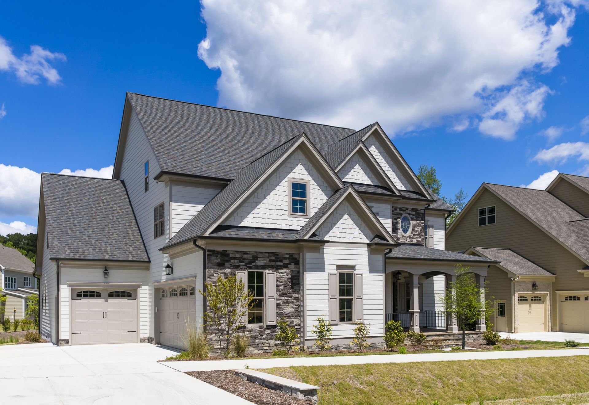 Modern two-story gray house with white trim, garage, and front porch under a blue sky