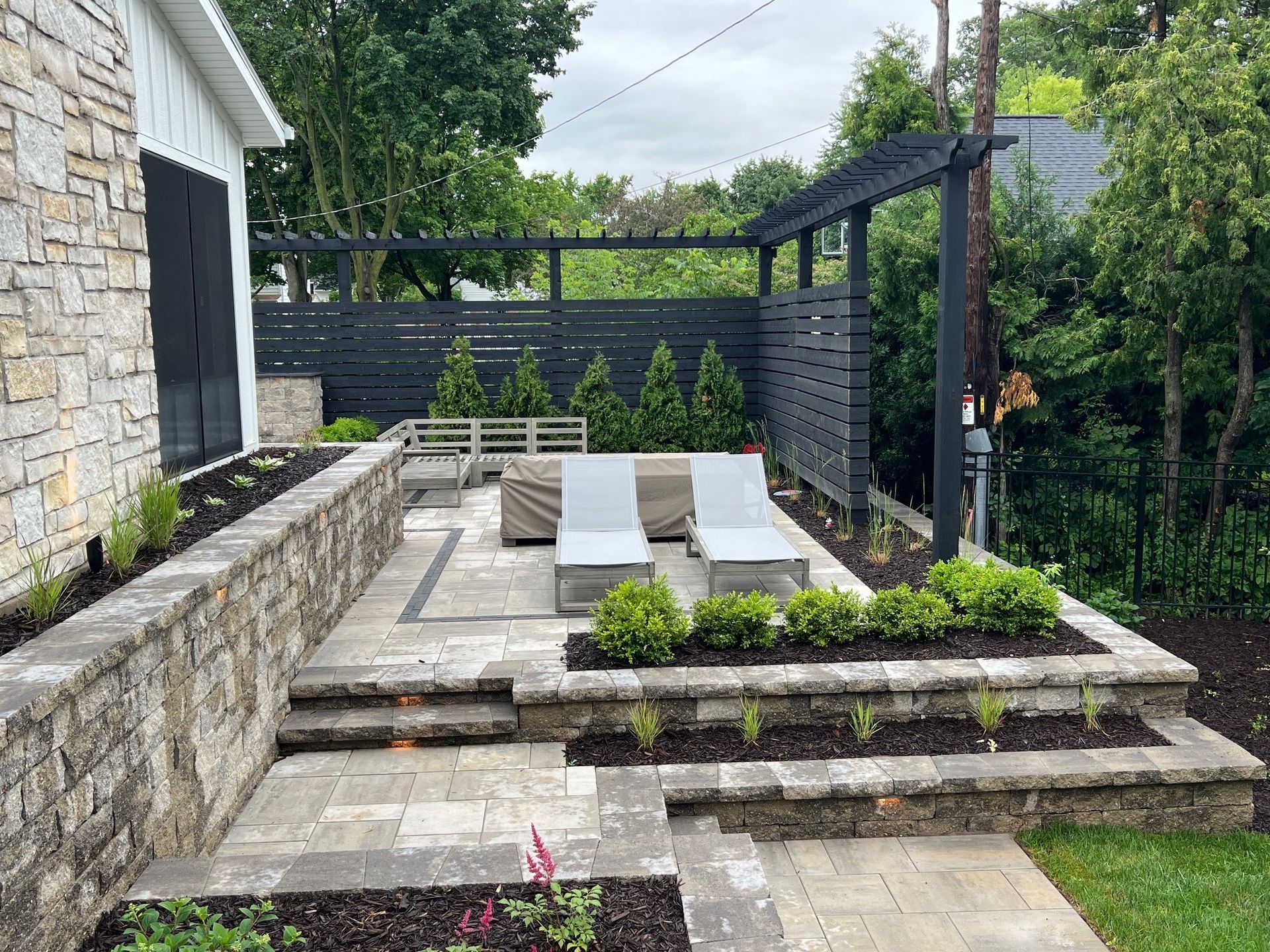 A patio with chairs and a pergola in the backyard of a house