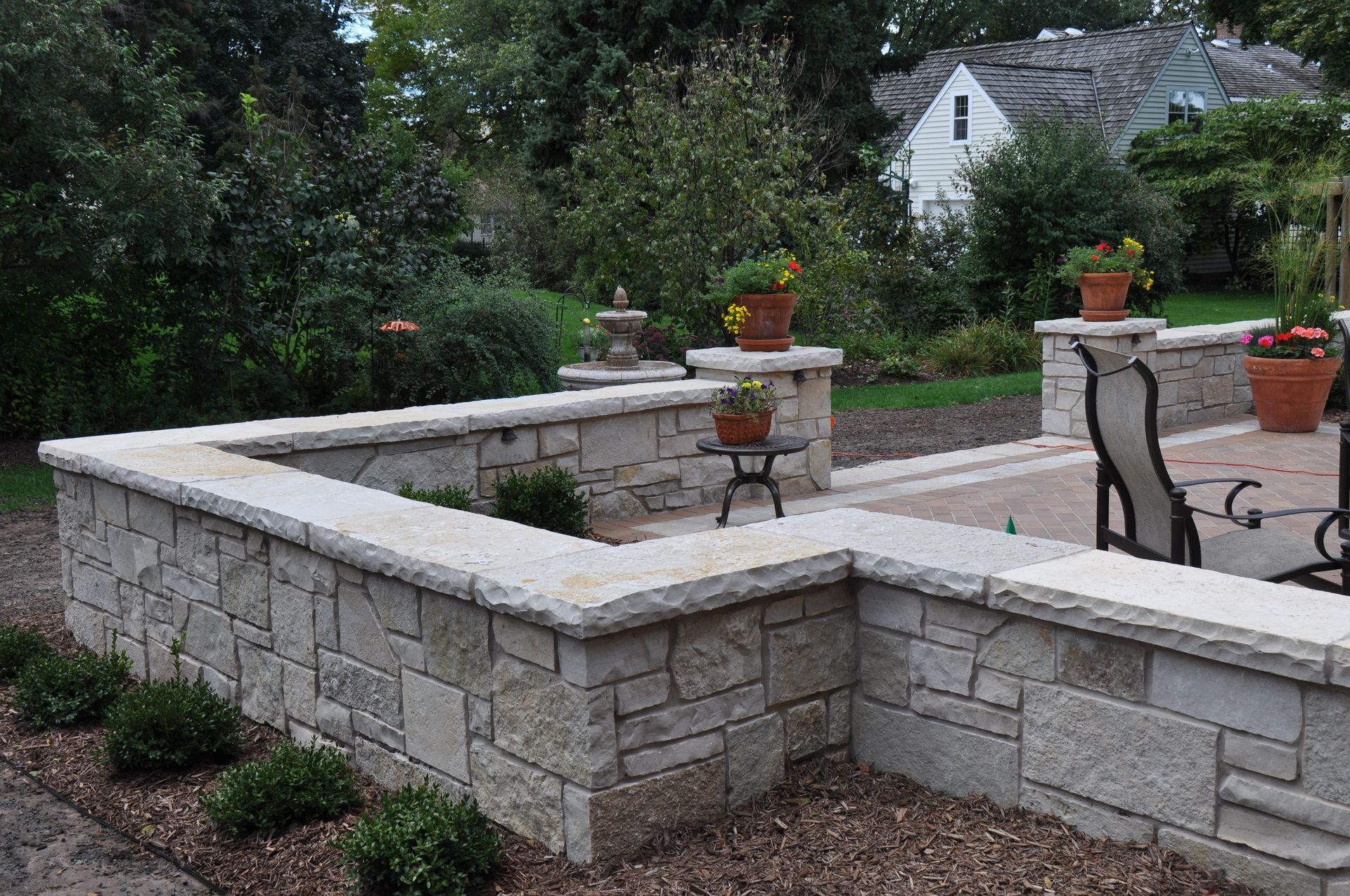 A stone wall surrounds a patio with a table and chairs