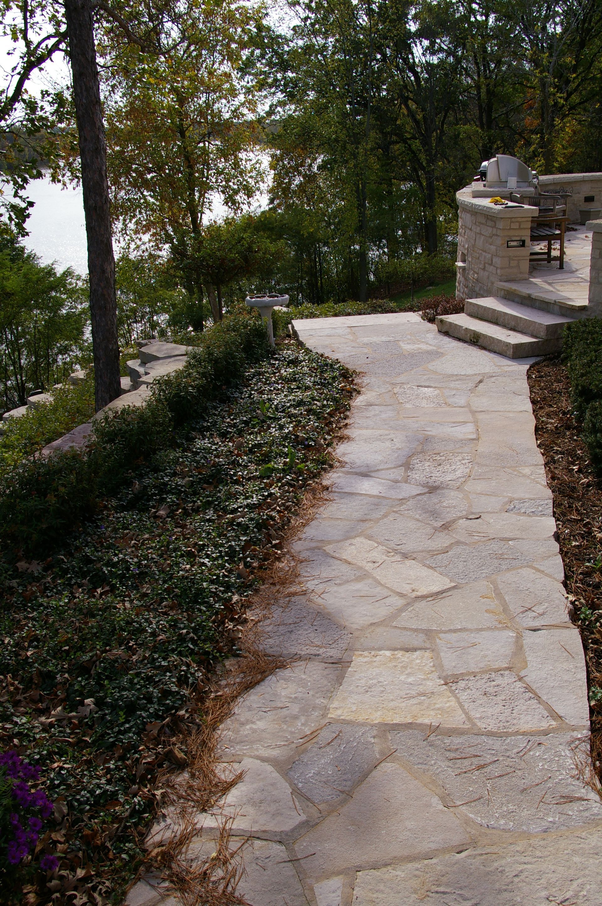 A stone walkway leading to a patio with a view of a lake
