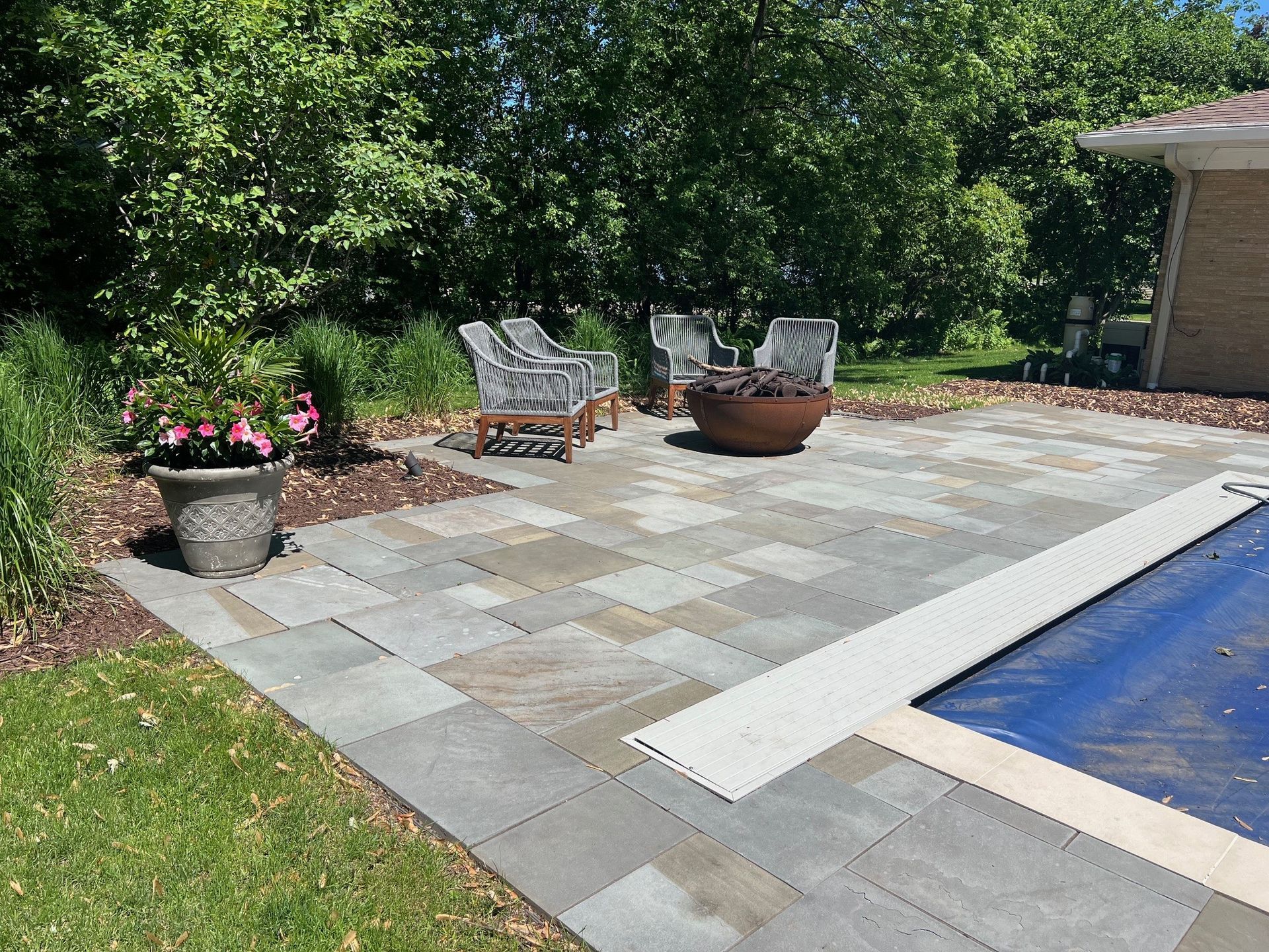 A patio with chairs and a fire pit next to a swimming pool