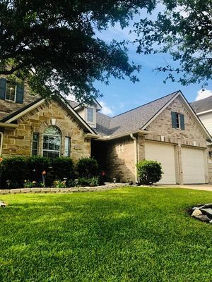 Two-story house with a stone facade and attached garage, set against a blue sky and green lawn.