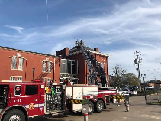 Fire truck with ladder extended to the roof of a red brick building; firefighters are on the roof.