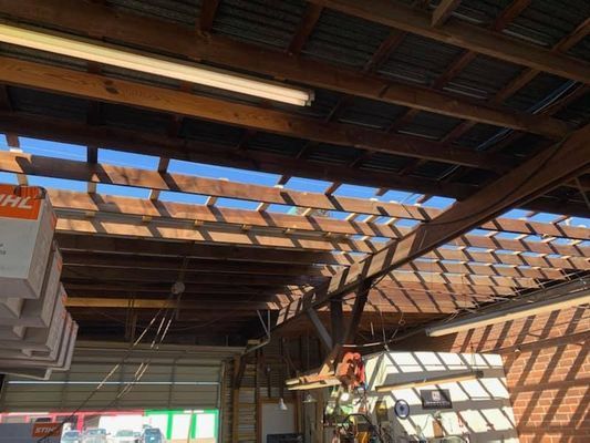 View of a workshop ceiling with wooden beams and partial roofing, sunlight streaming through the openings.