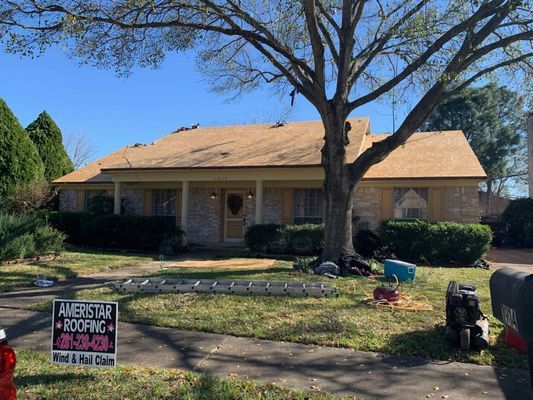House with partially removed roof, construction debris, and a company sign. Clear blue sky, sunny day.