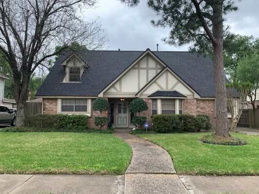 A brick and stucco Tudor-style house with a dark gray roof, a green lawn, and a curved sidewalk.