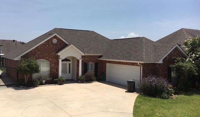 Brick house with a dark gray roof, white garage door, and a concrete driveway on a sunny day.