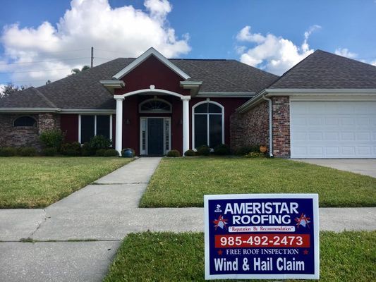 A house with a new roof, a sign from Ameristar Roofing displays contact information and wind and hail claim services.