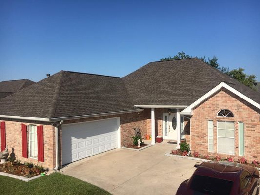 Brick house with a brown shingled roof, white garage door, and red shutters against a clear blue sky.