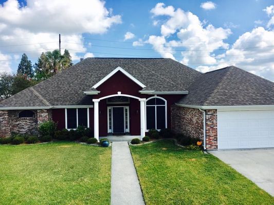 A one-story brick house with a gray roof, a red front door, and a white garage door under a blue sky.