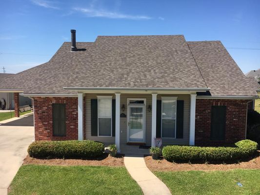 Brick and gray-roofed house with a white-columned porch, green lawn, and a clear blue sky.