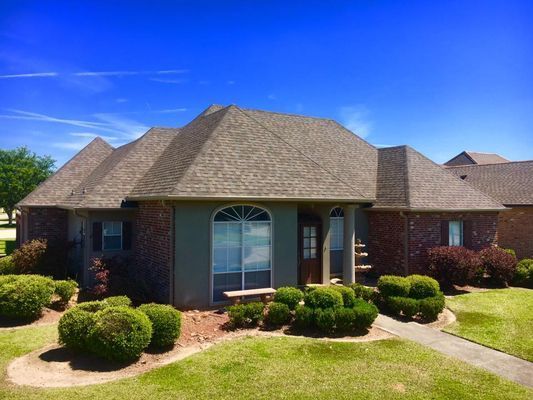 A one-story brick home with a brown roof and landscaping against a bright blue sky.