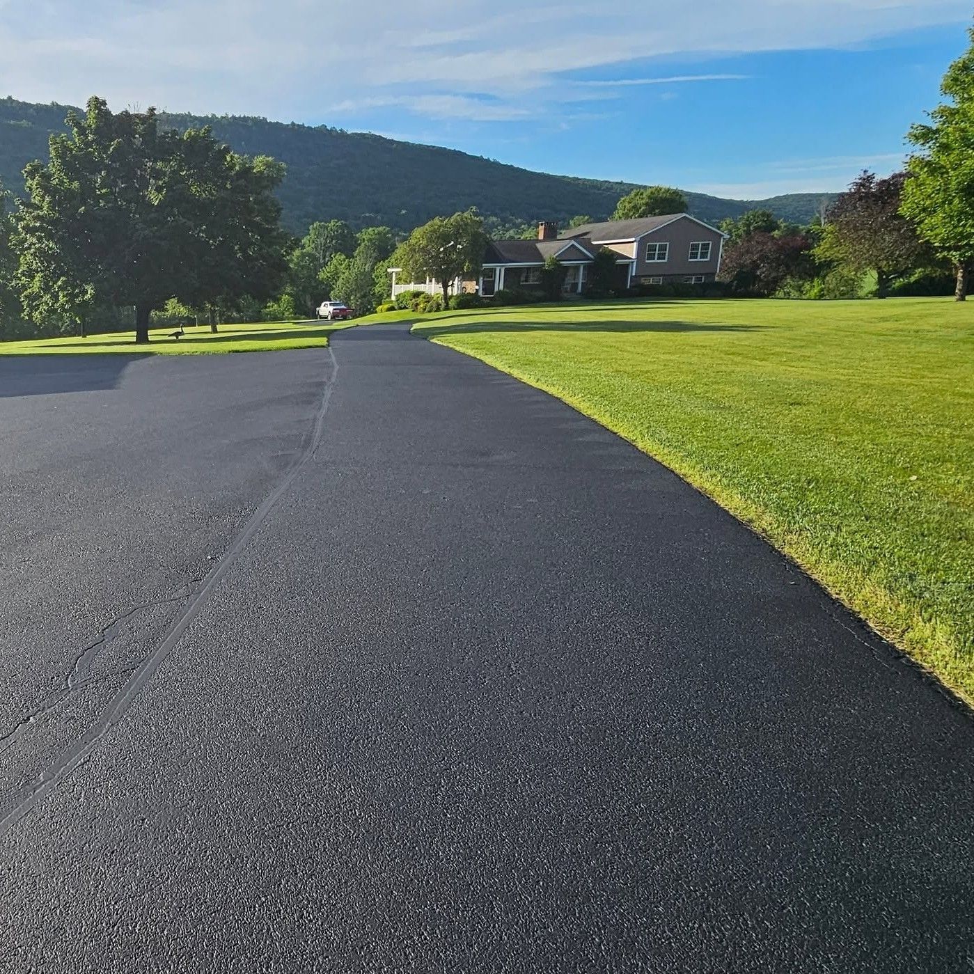 Freshly paved driveway beside a green lawn, with houses and hills under a clear blue sky