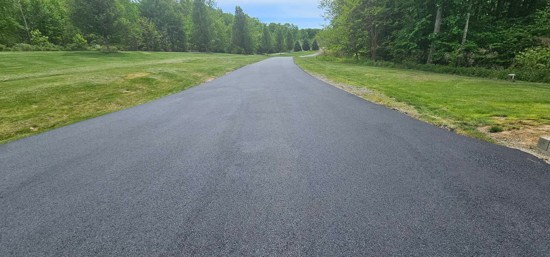Paved road stretching through a green wooded landscape under a bright sky