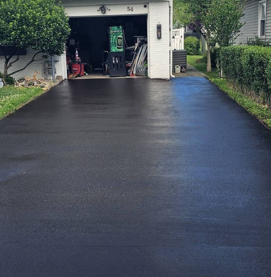 Freshly paved black driveway leading to an open garage beside a house