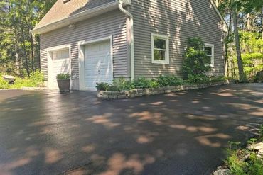 Detached garage with white doors beside a freshly paved driveway and surrounding trees