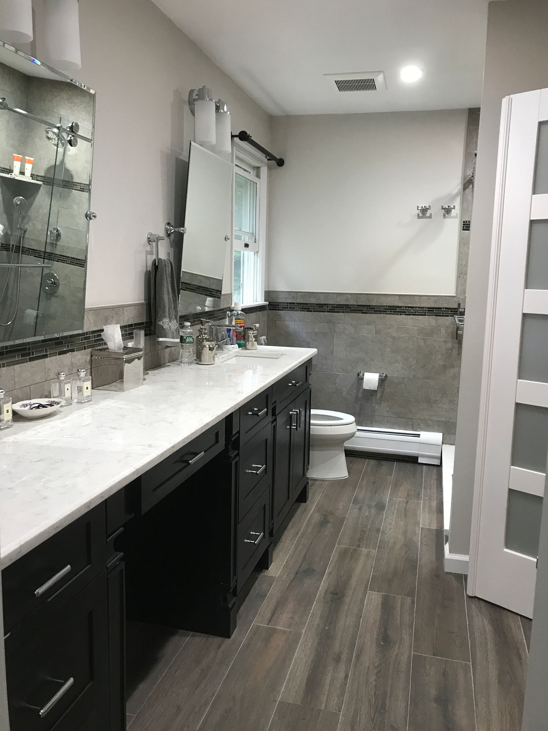 Bathroom with white vanity, dark cabinets, glass shelves, and a toilet beside a tiled shower area