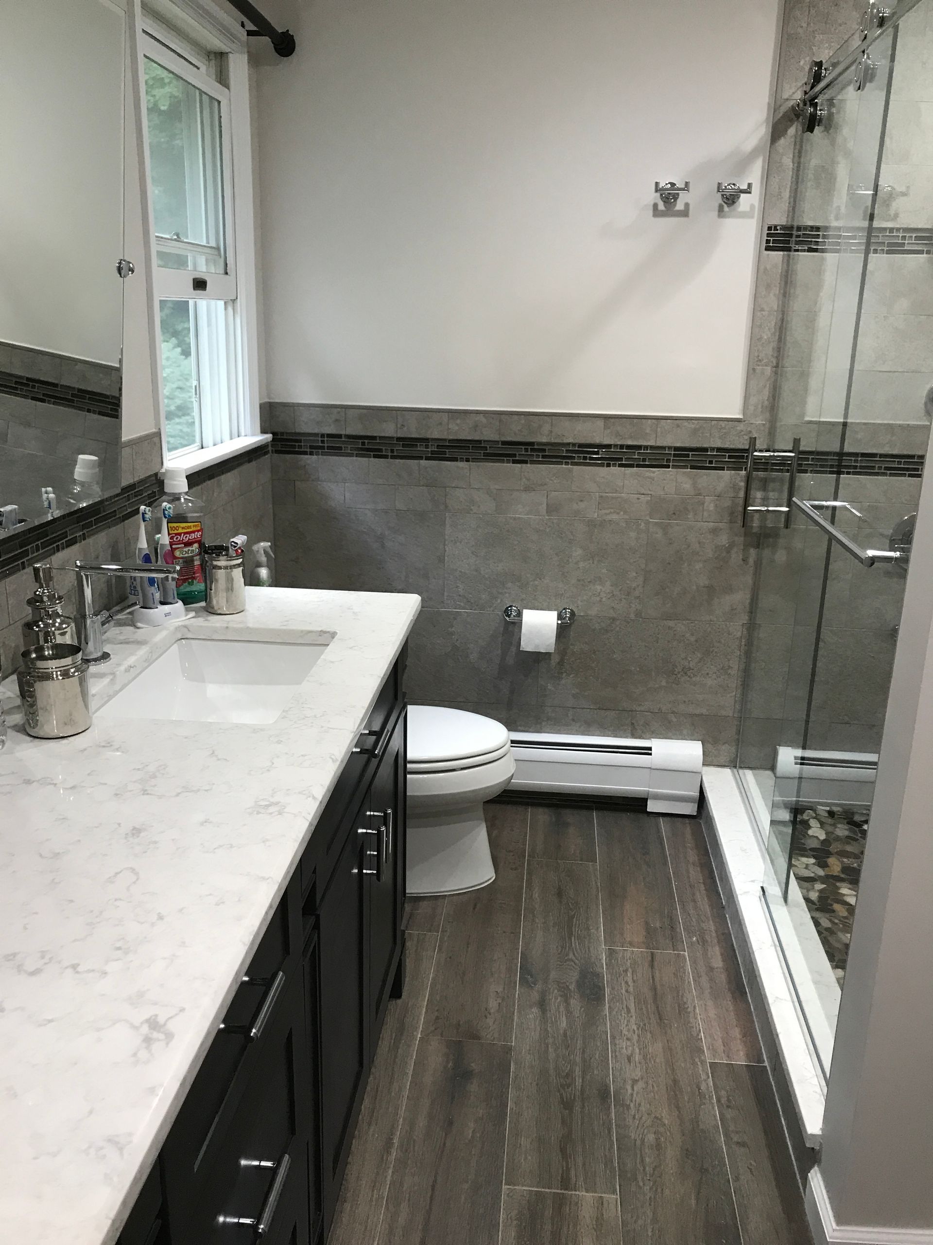 Modern bathroom with white vanity, dark wood floor, glass shower, and toilet against gray walls