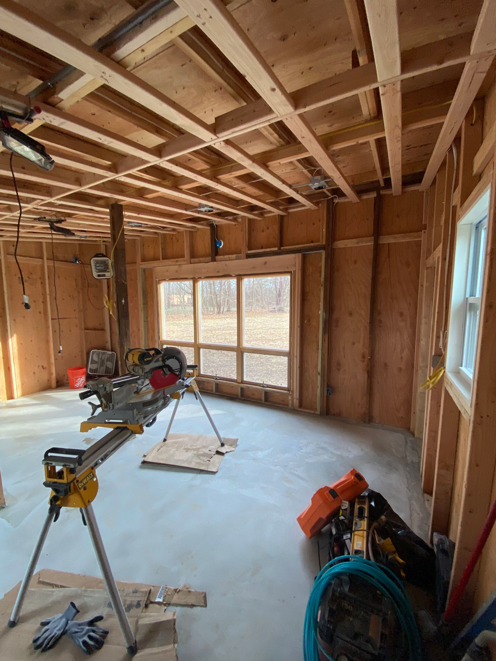 Unfinished room with exposed wood framing, a concrete floor, and construction tools near windows.