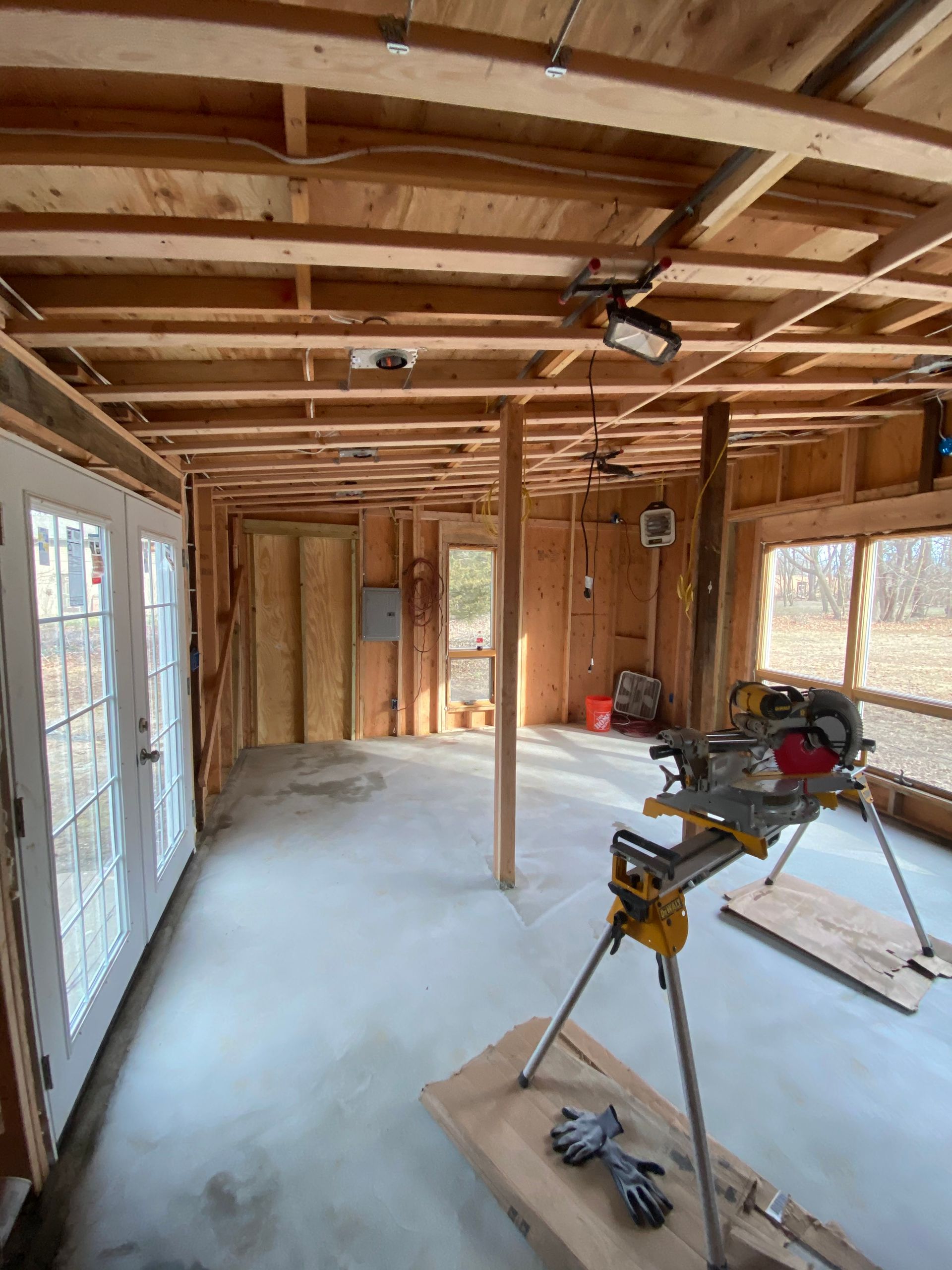 Unfinished room with exposed wood framing, concrete floor, windows, and construction tools on stands